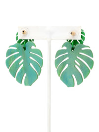 A pair of green monstera leaf drop earrings displayed on a white T-shaped jewelry stand against a white. background.