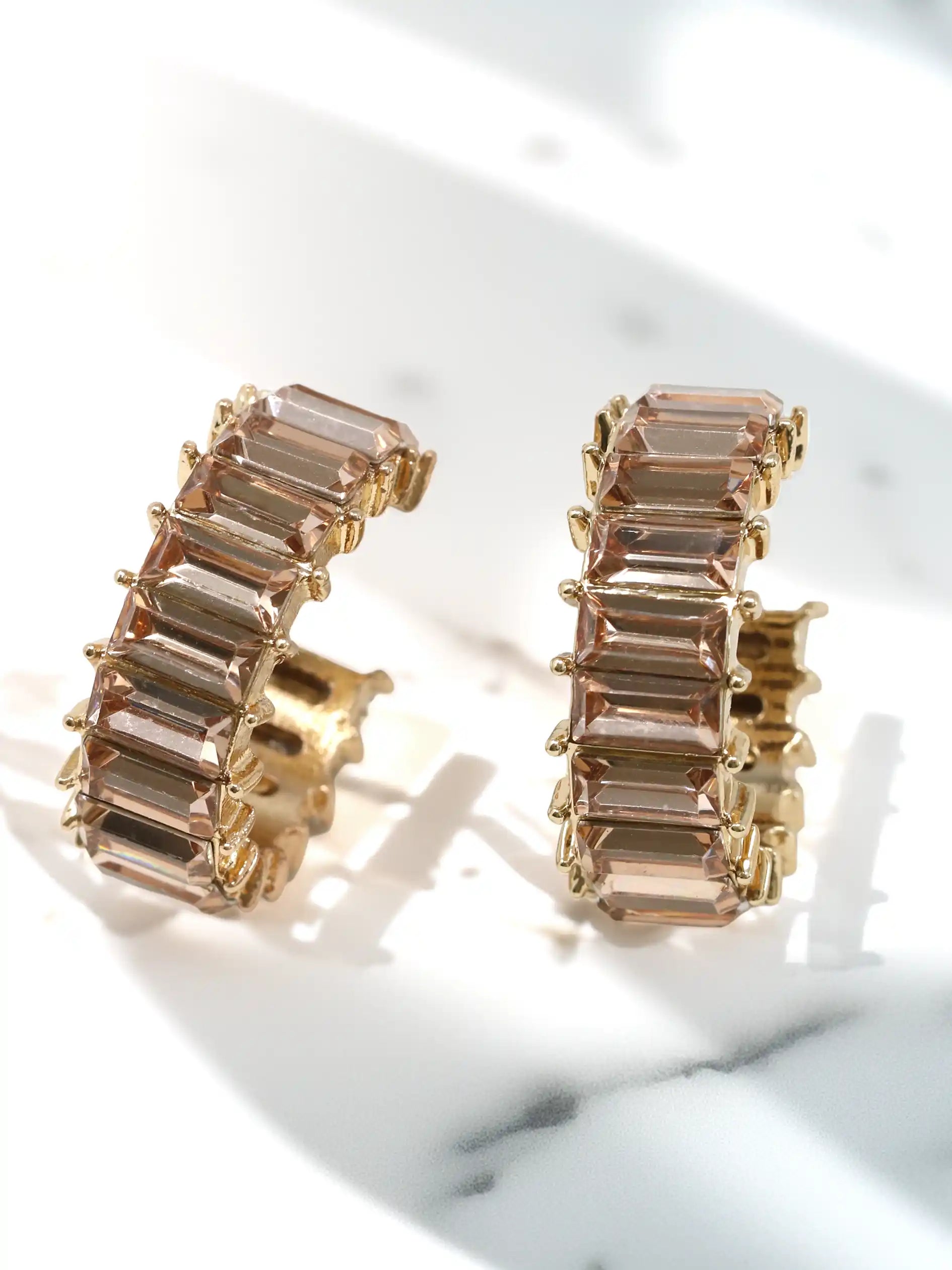 Gold hoop earrings with champagne glass stones on a marble surface