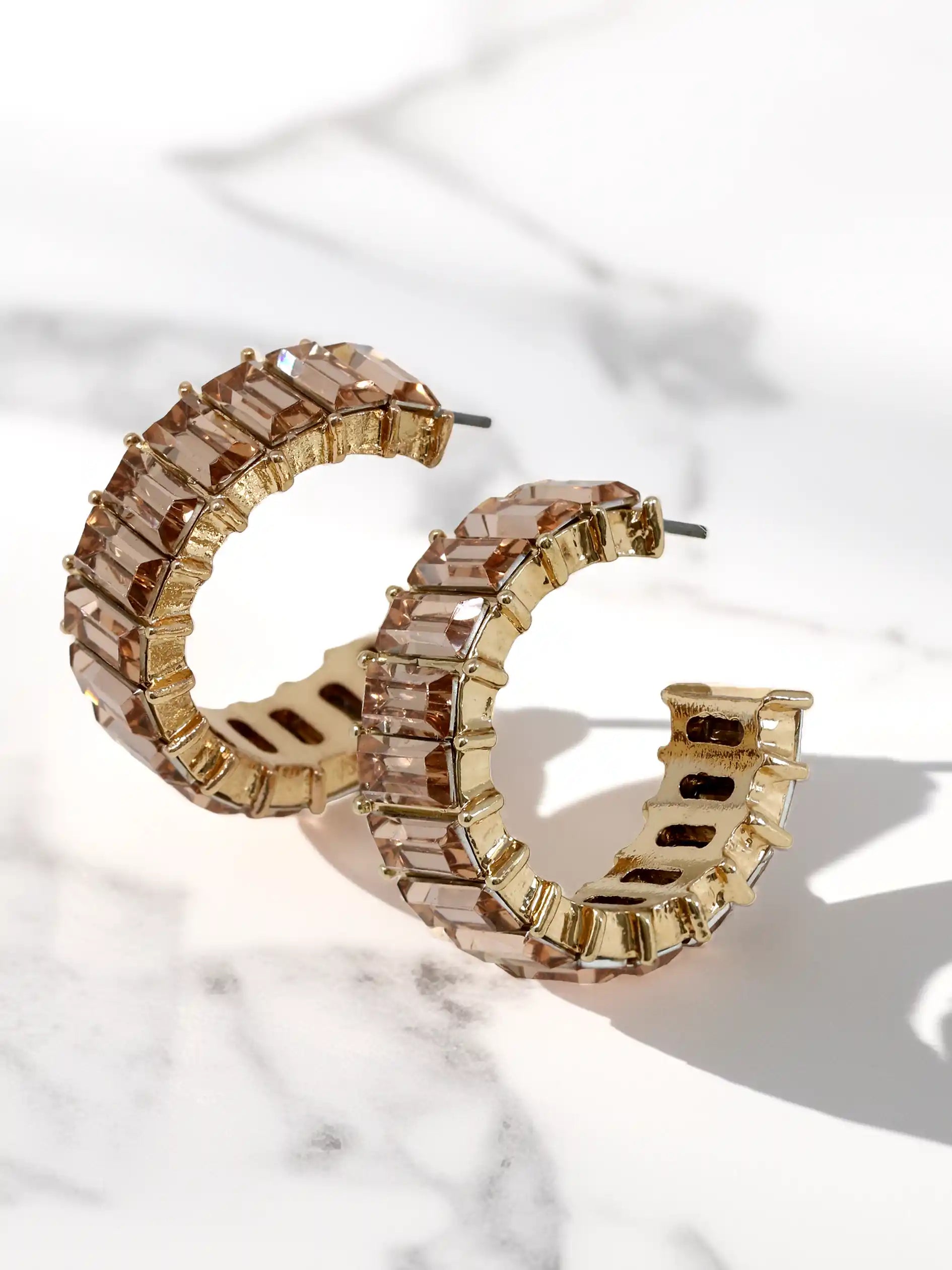Gold hoop earrings with champagne glass stones on a marble surface