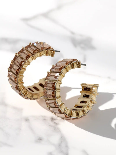 Gold hoop earrings with champagne glass stones on a marble surface