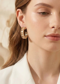 Close-up of a woman wearing gold hoop earrings with a neutral background