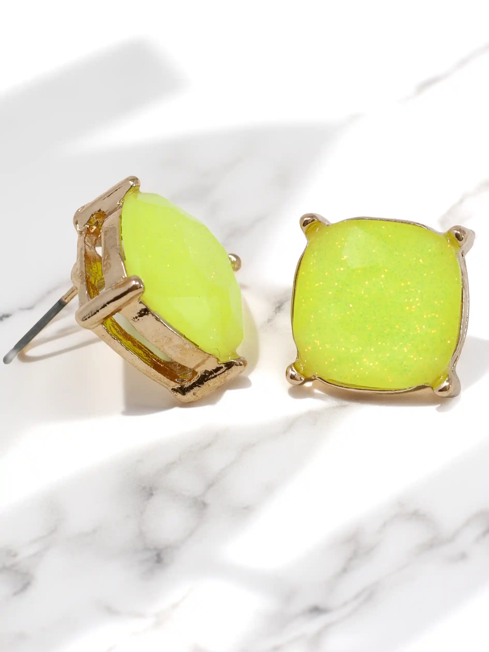 Neon green earrings with gold accents on a marble surface