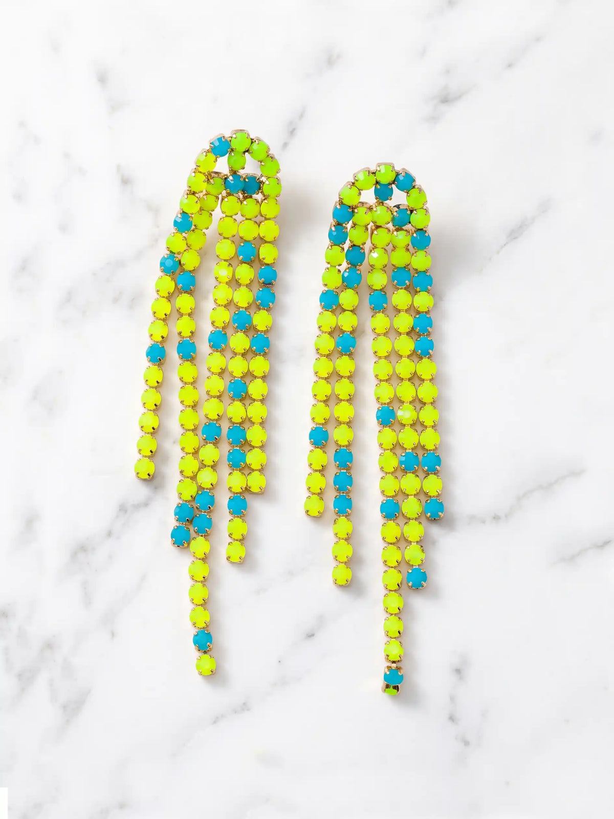 Overhead shot of a pair of long, cascading duster earrings featuring tiered strands of vibrant neon yellow-green and bright turquoise-blue faceted beads set in gold-tone metal. The earrings are lying flat on a white marble surface.