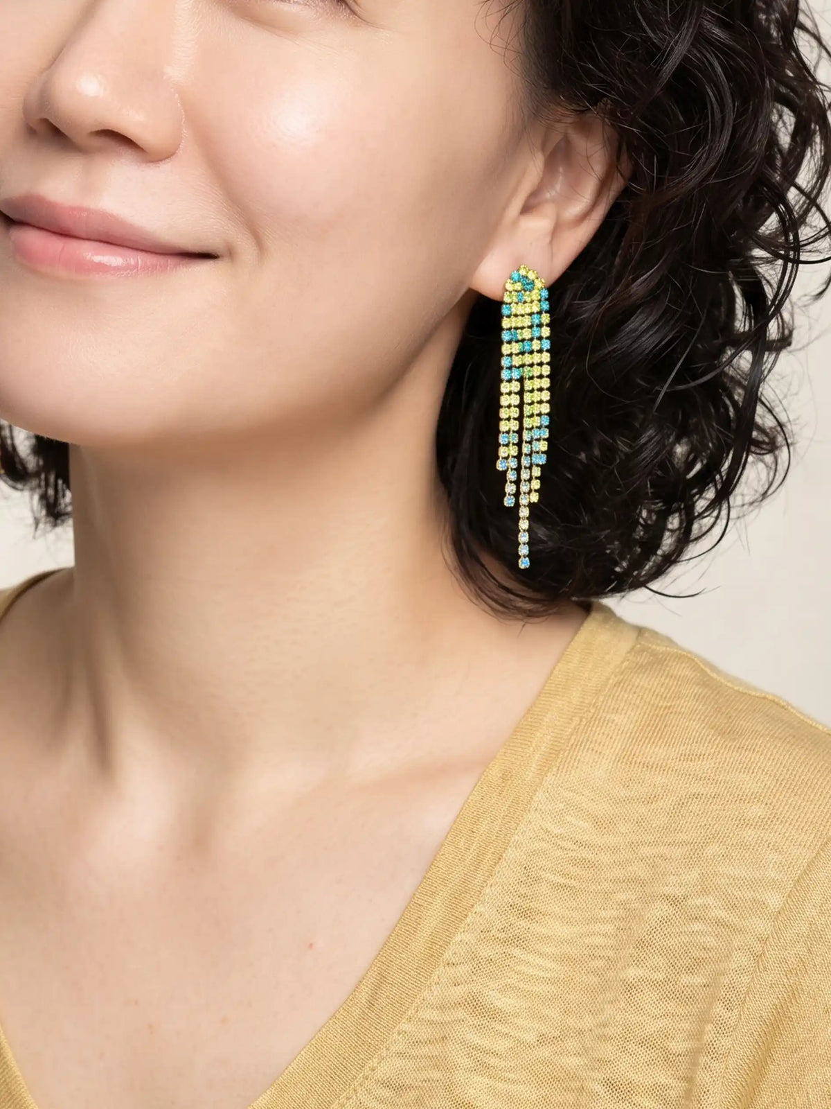 Overhead shot of a pair of long, cascading duster earrings featuring tiered strands of vibrant neon yellow-green and bright turquoise-blue faceted beads set in gold-tone metal.