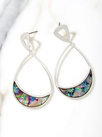 A pair of silver teardrop dangle earrings with a crescent-shaped iridescent abalone shell inlay, displayed on a white marble surface.