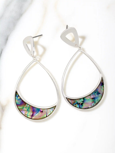 A pair of silver teardrop dangle earrings with a crescent-shaped iridescent abalone shell inlay, displayed on a white marble surface.