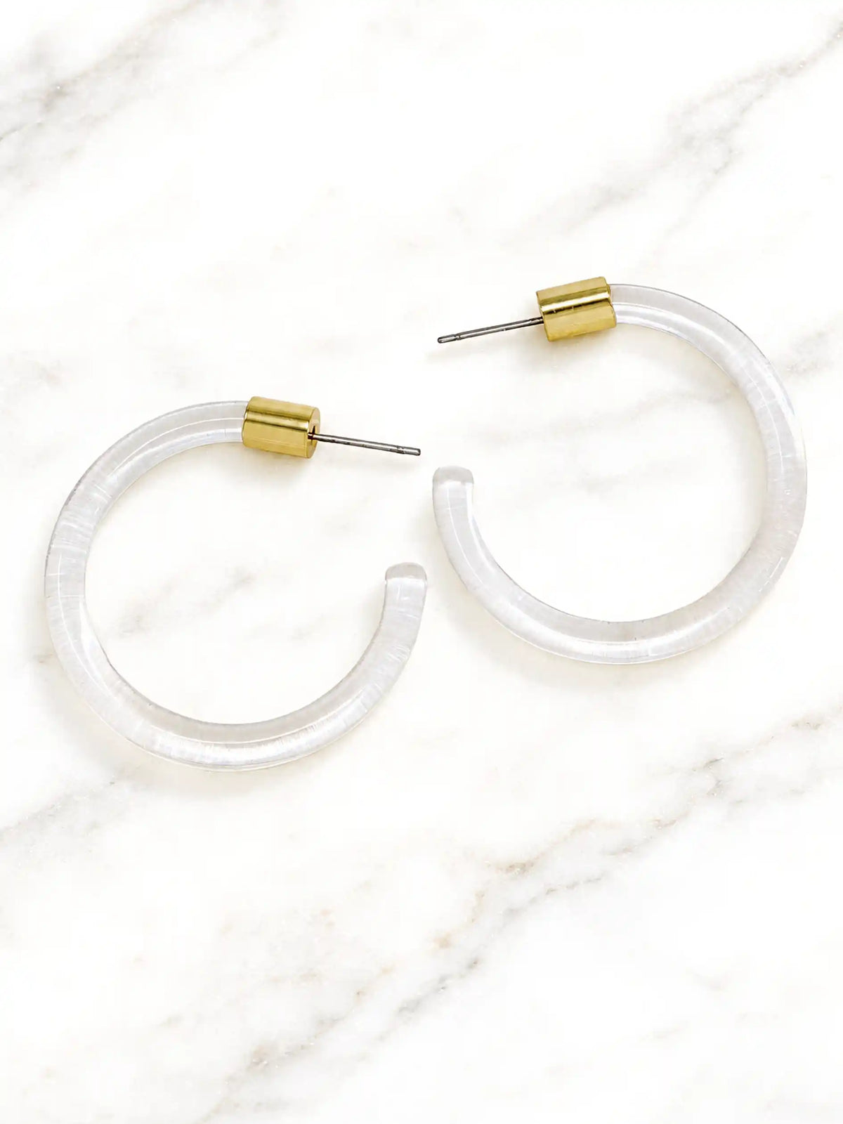 Pair of clear Lucite hoop earrings by Bauble Sky featuring polished transparent resin, gold-tone accents, and a modern minimalist design.