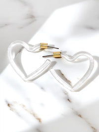 Clear heart-shaped lucite hoop earrings with a polished transparent resin finish and gold-tone metal accents, displayed on a white background.