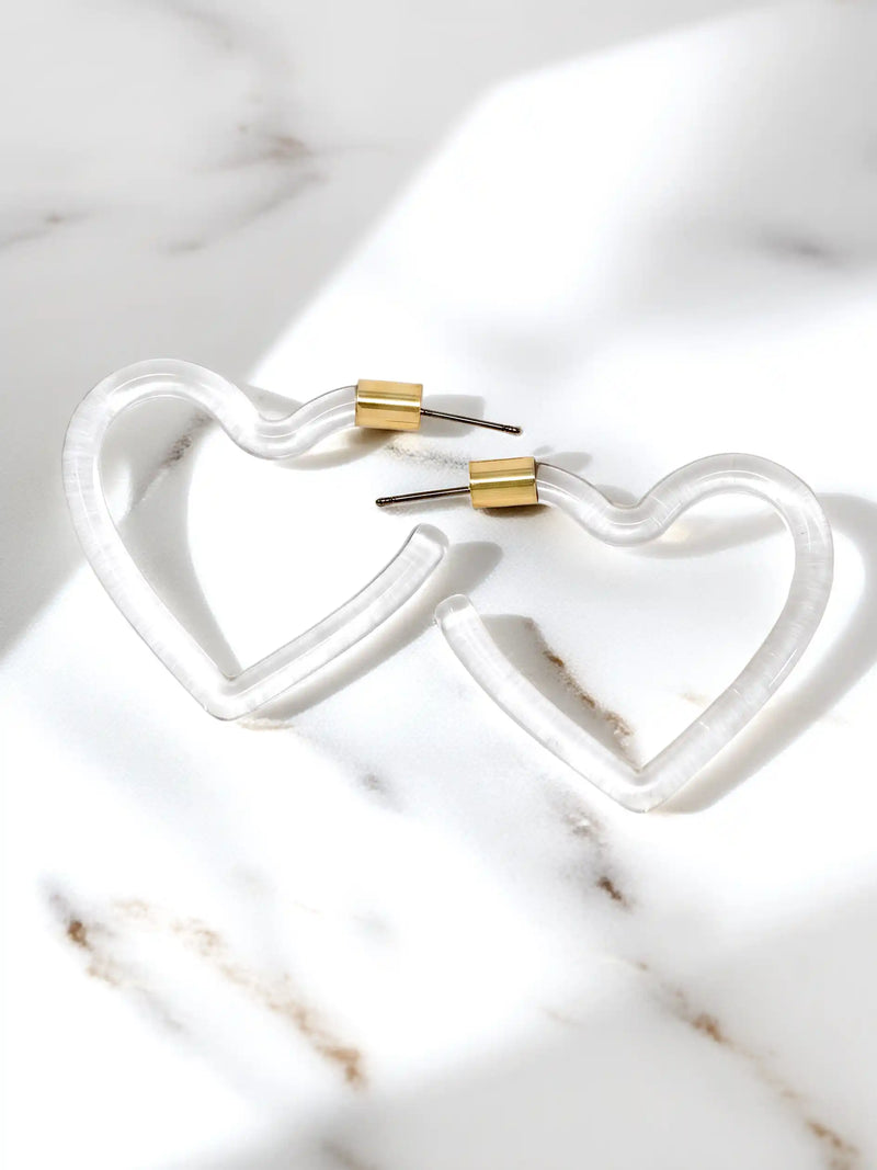 Clear heart-shaped lucite hoop earrings with a polished transparent resin finish and gold-tone metal accents, displayed on a white background.