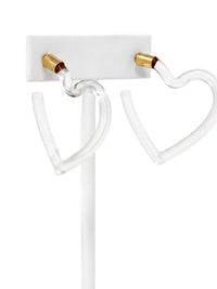 Clear acrylic heart-shaped hoop earrings with gold-colored post caps, displayed on a white stand against a white background.