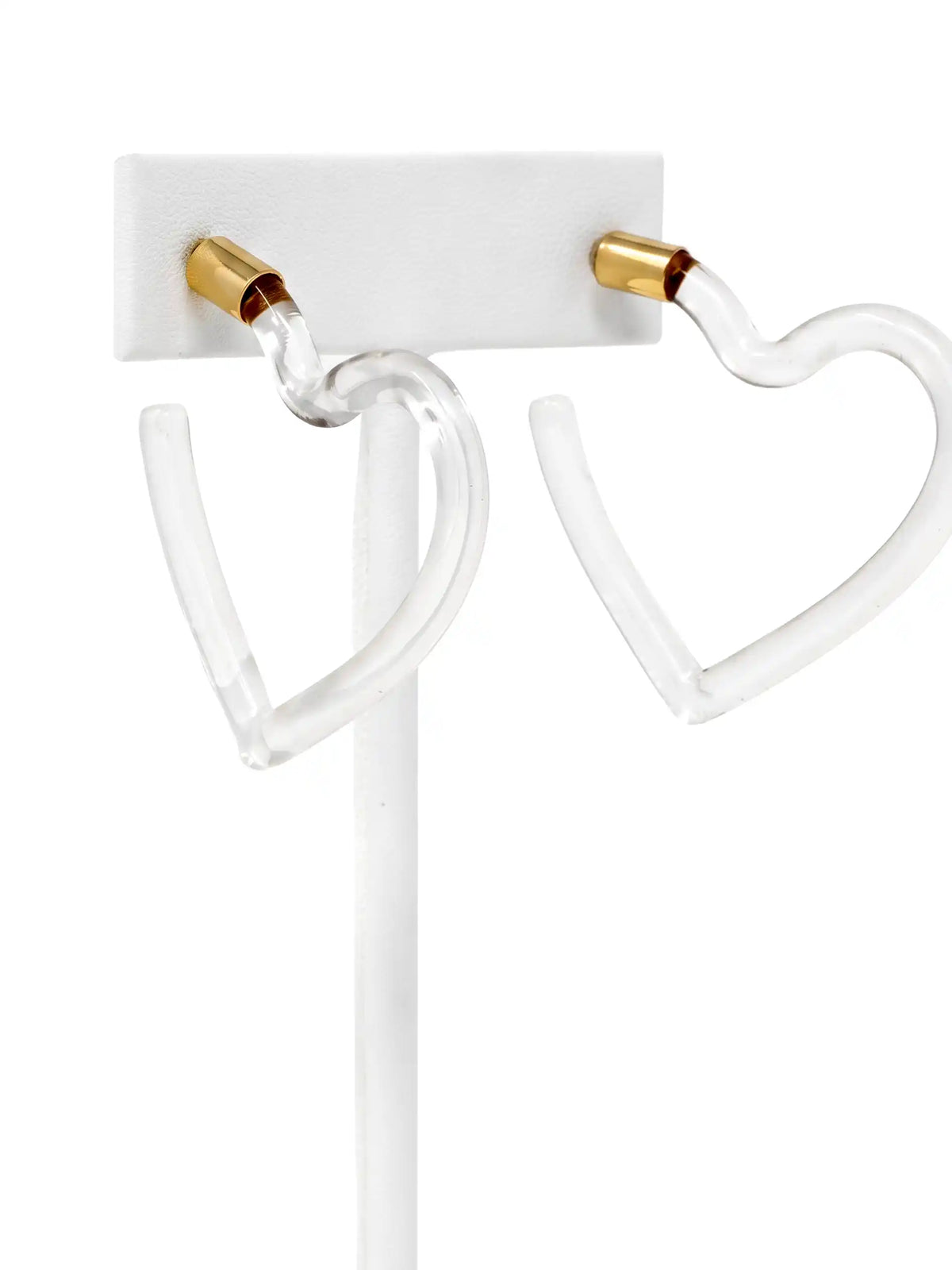 Clear acrylic heart-shaped hoop earrings with gold-colored post caps, displayed on a white stand against a white background.