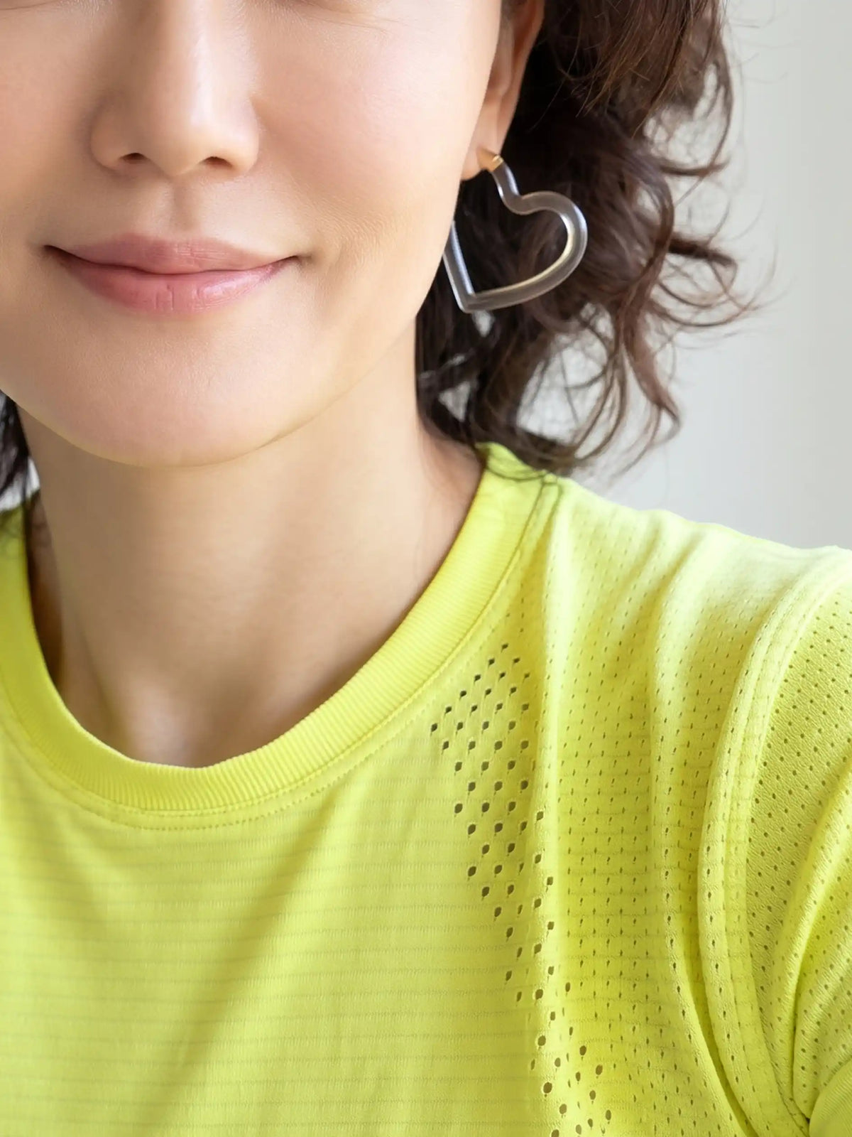 Close-up of a woman wearing a bright yellow-green athletic t-shirt and a clear resin heart-shaped earring.
