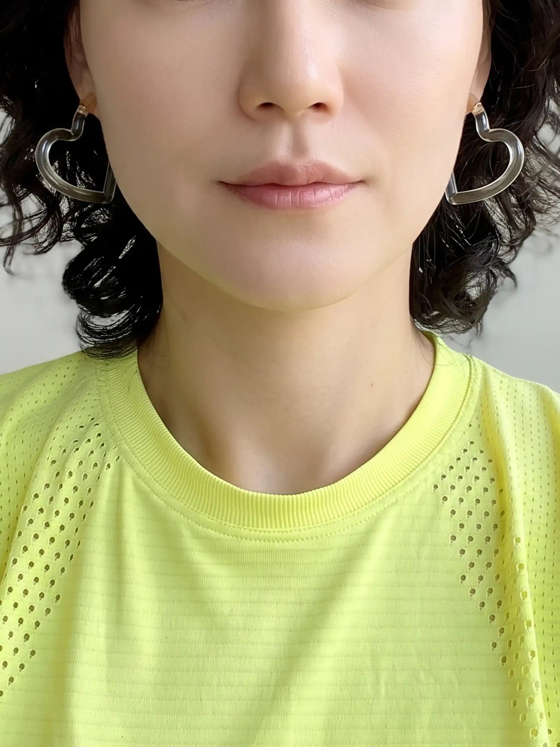 Close-up of a woman wearing a bright yellow-green athletic t-shirt and a clear resin heart-shaped earring.