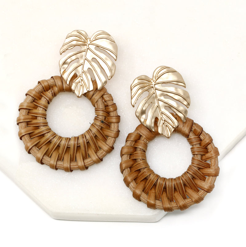 A pair of elegant circle rattan earrings with a decorative metal leaf accentuating the top.