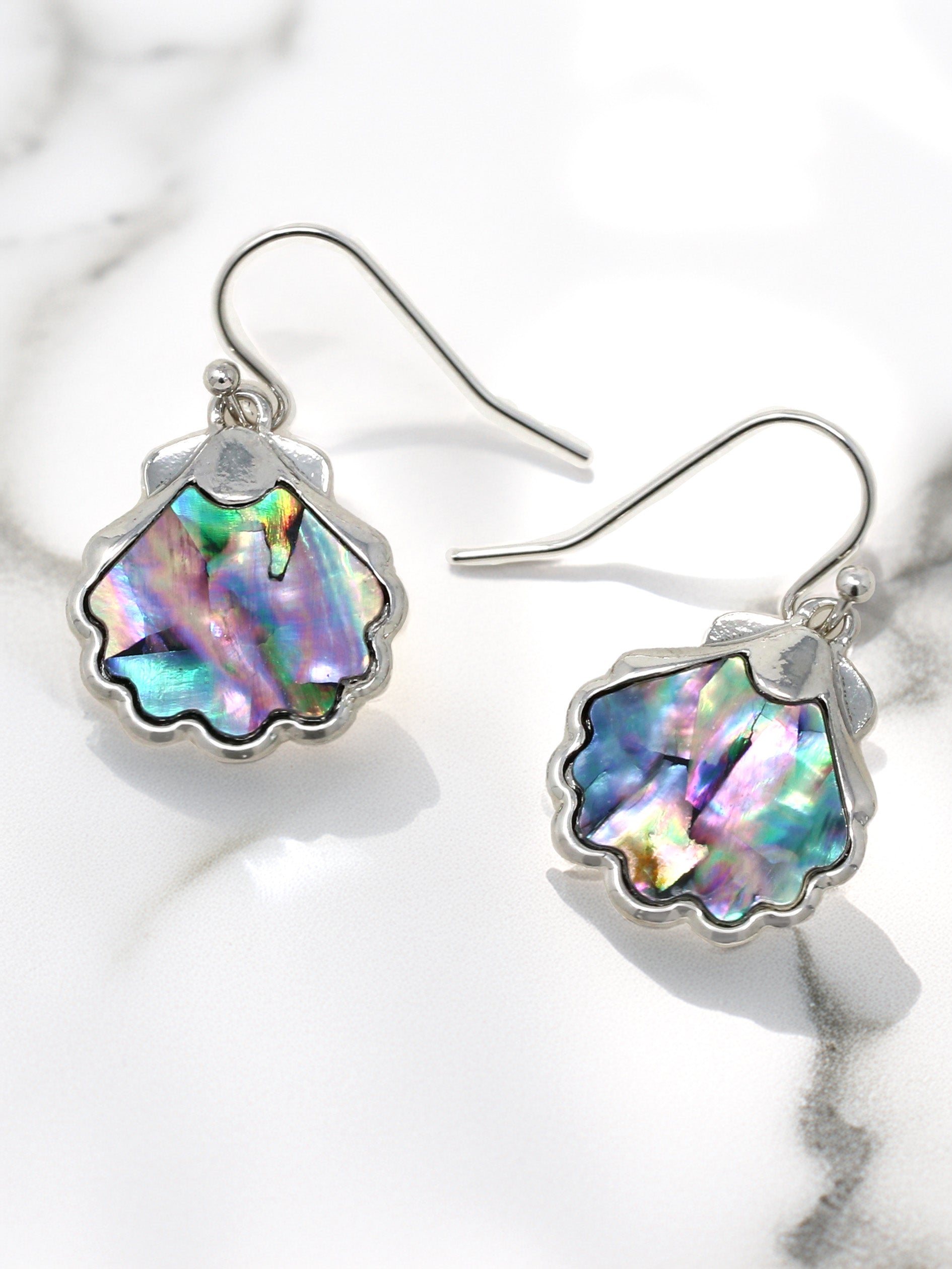 Shell-shaped earrings with colorful interior on a marble surface