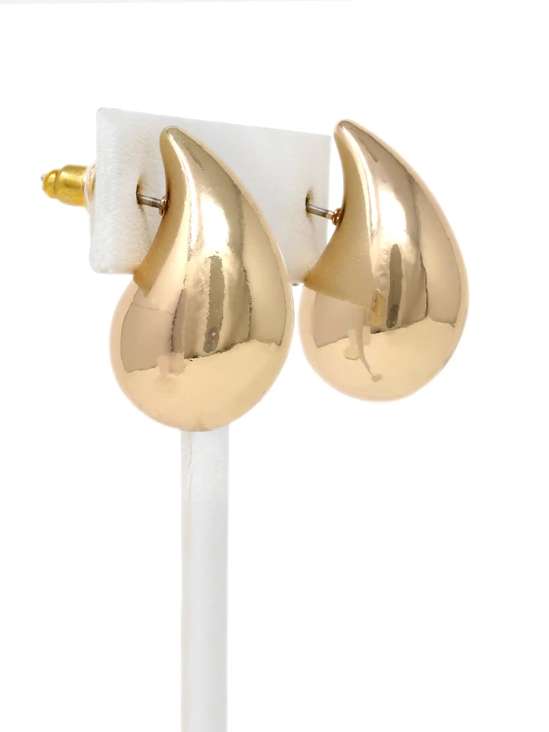 A pair of gold teardrop-shaped hoop earrings displayed on a white jewelry stand against a white background.