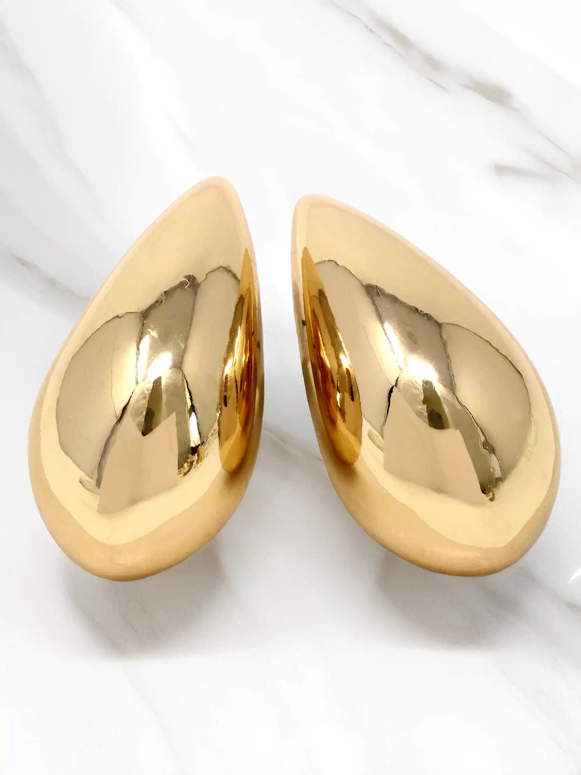 A pair of teardrop-shaped, highly polished gold wall art pieces displayed on a white marble surface.