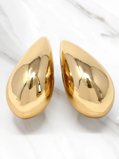 A pair of teardrop-shaped, highly polished gold wall art pieces displayed on a white marble surface.