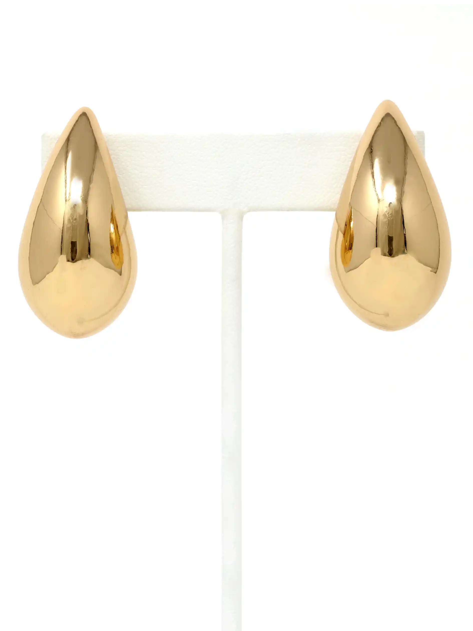A pair of polished gold teardrop-shaped stud earrings displayed on a white T-shaped jewelry stand against a white background.