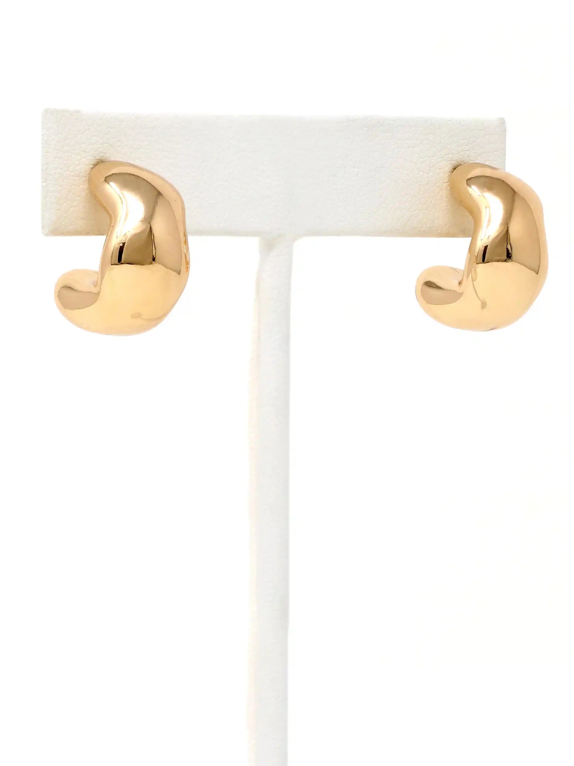 A pair of polished gold huggie hoop earrings displayed on a white jewelry stand against a white background.