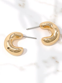 A pair of gold crescent-shaped hoop earrings with silver post backs, displayed on a white marble surface.