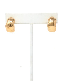 A pair of gold-colored, irregularly shaped hoop earrings displayed on a white T-stand against a white background.
