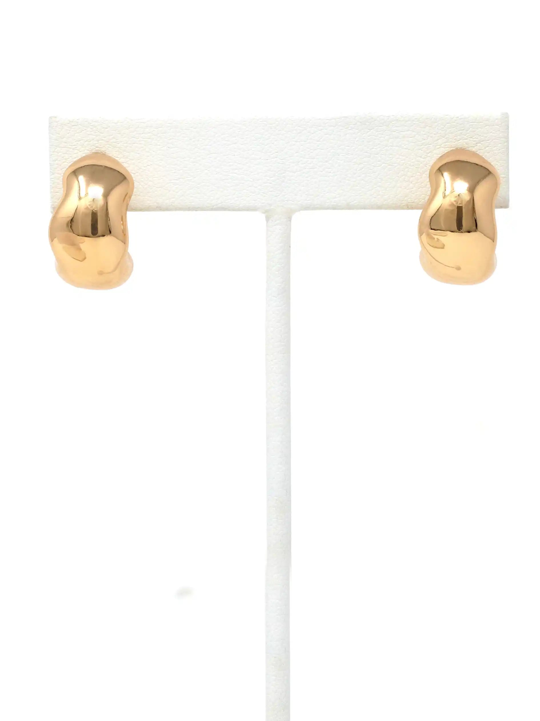 A pair of gold-colored, irregularly shaped hoop earrings displayed on a white T-stand against a white background.