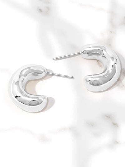 A pair of polished silver crescent-shaped hoop earrings with post backs, displayed on a white marble surface.