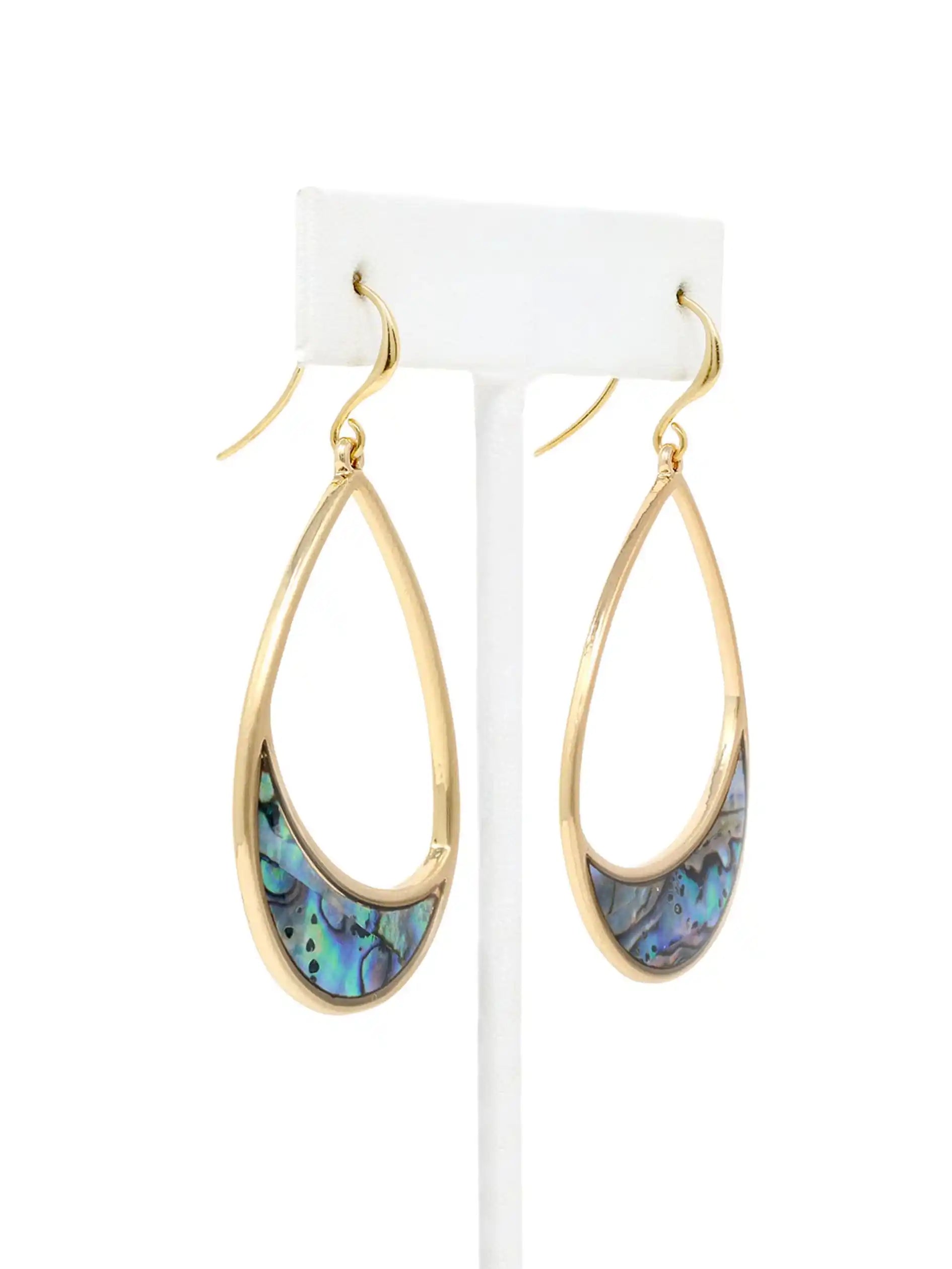 A pair of gold teardrop dangle earrings with iridescent abalone shell inlays, displayed on a white stand against a white background.