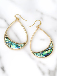 A pair of gold teardrop-shaped dangle earrings with a crescent-shaped abalone shell inlay, displayed on a white marble background.