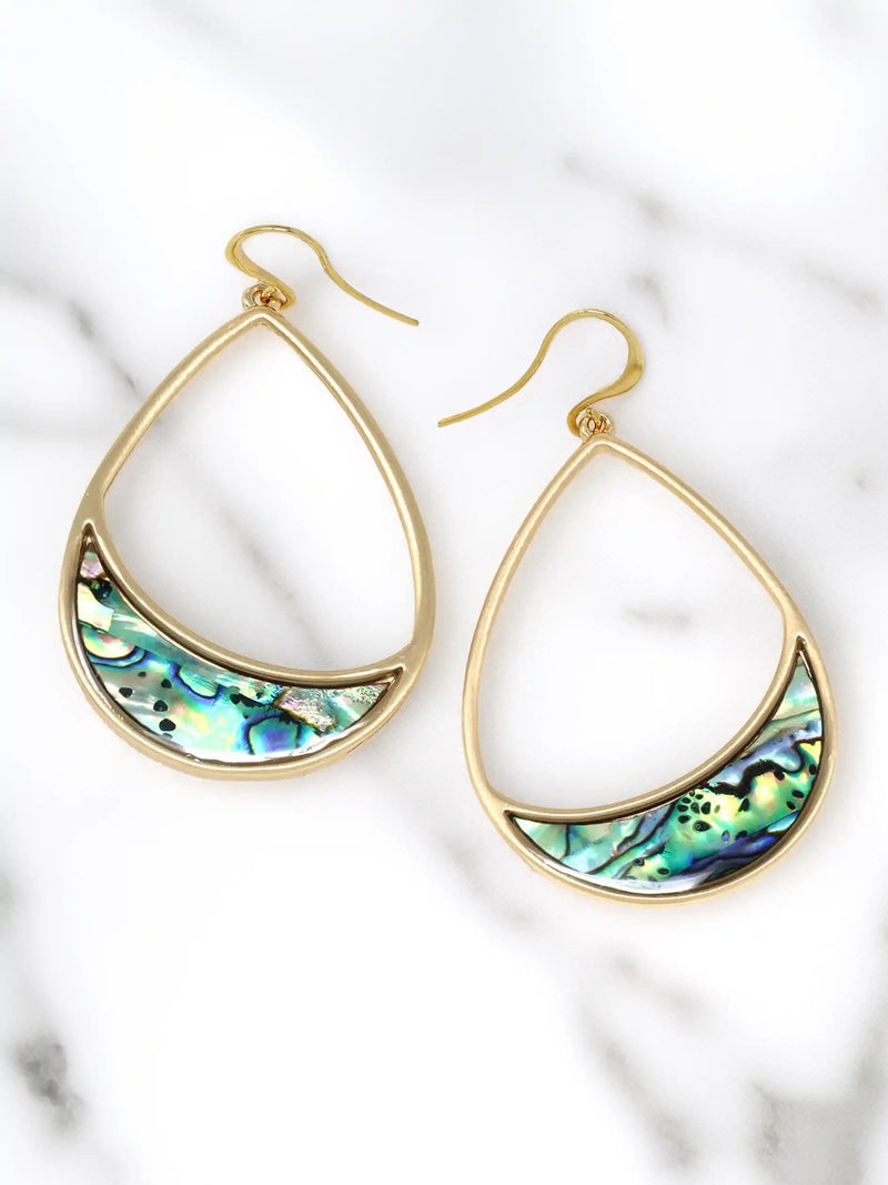 A pair of gold teardrop-shaped dangle earrings with a crescent-shaped abalone shell inlay, displayed on a white marble background.