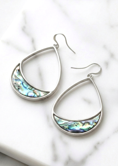Silver earrings with abalone shell inlay on a marble surface