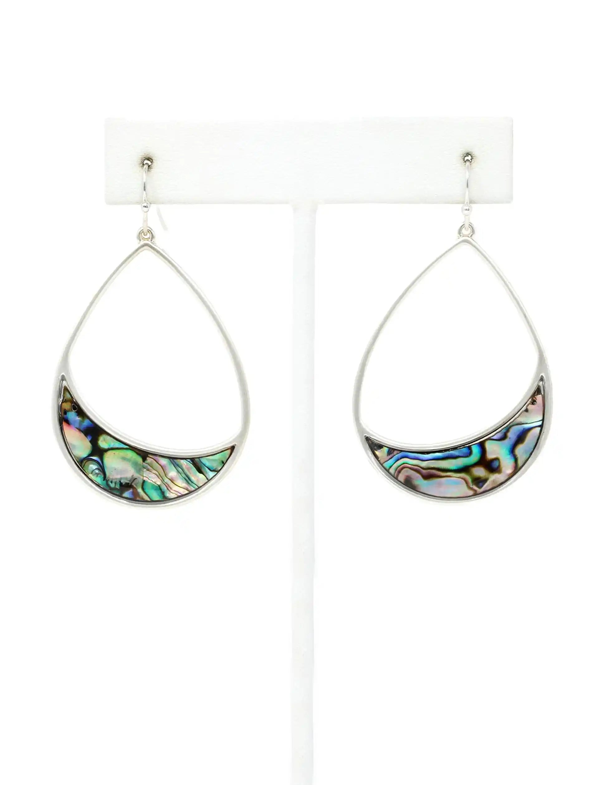 A pair of silver teardrop dangle earrings with crescent-shaped abalone shell inlays, displayed on a white jewelry stand against a white background.
