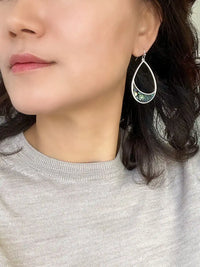 A pair of silver teardrop-shaped dangle earrings with a crescent-shaped abalone shell inlay.
