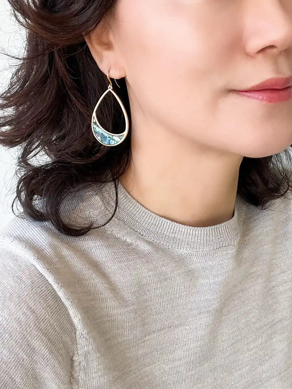 A pair of gold teardrop-shaped dangle earrings with a crescent-shaped abalone shell inlay.