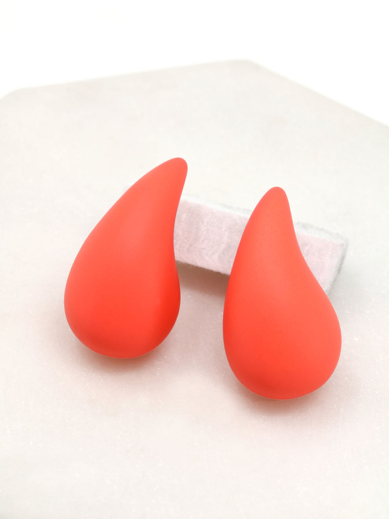 A close-up of neon orange puffy hollow teardrop earrings, showcasing their modern and minimalist design. The earrings make a statement with their sleek metal construction and distinctive shape.