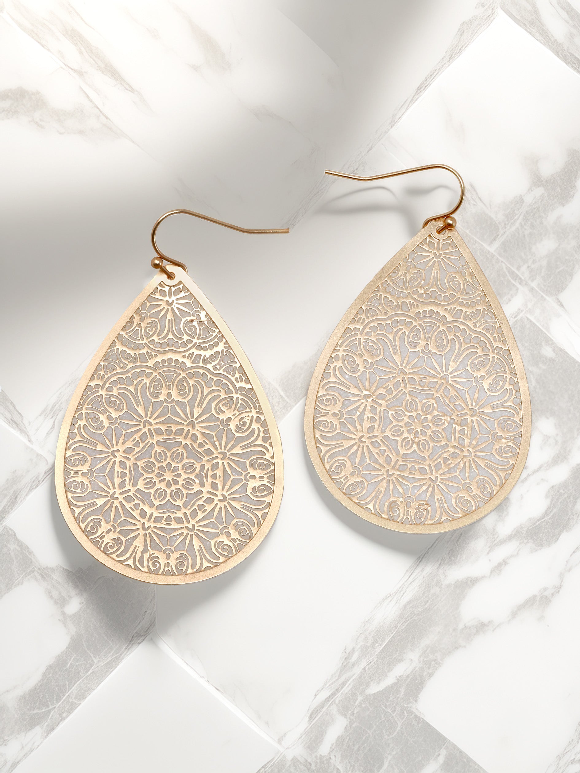 A pair of matte gold teardrop-shaped drop earrings with intricate filigree detailing.