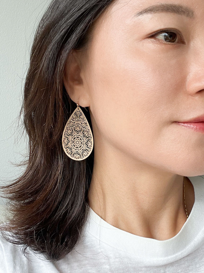 A pair of matte gold teardrop-shaped drop earrings with intricate filigree detailing.
