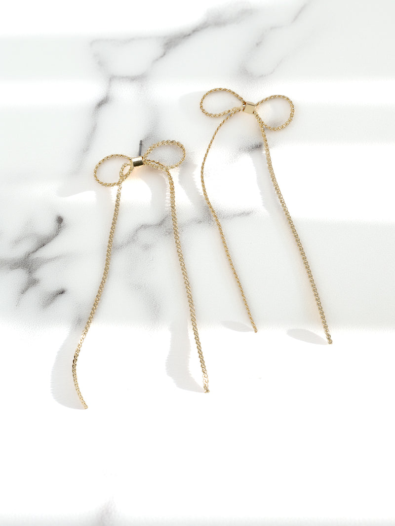 A pair of delicate gold-tone earrings with small ribbon bows at the top and long.