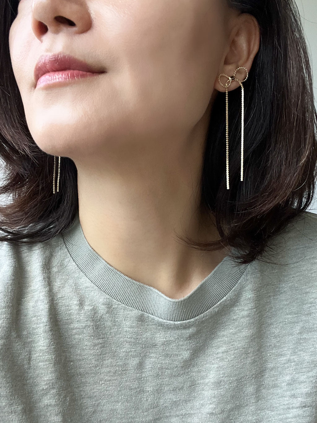 A pair of delicate gold-tone earrings with small ribbon bows at the top and long.