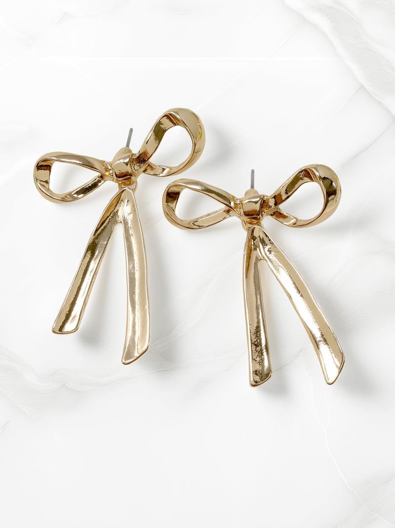 A pair of shiny gold-tone ribbon-shaped statement earrings with dangling lower ribbons.