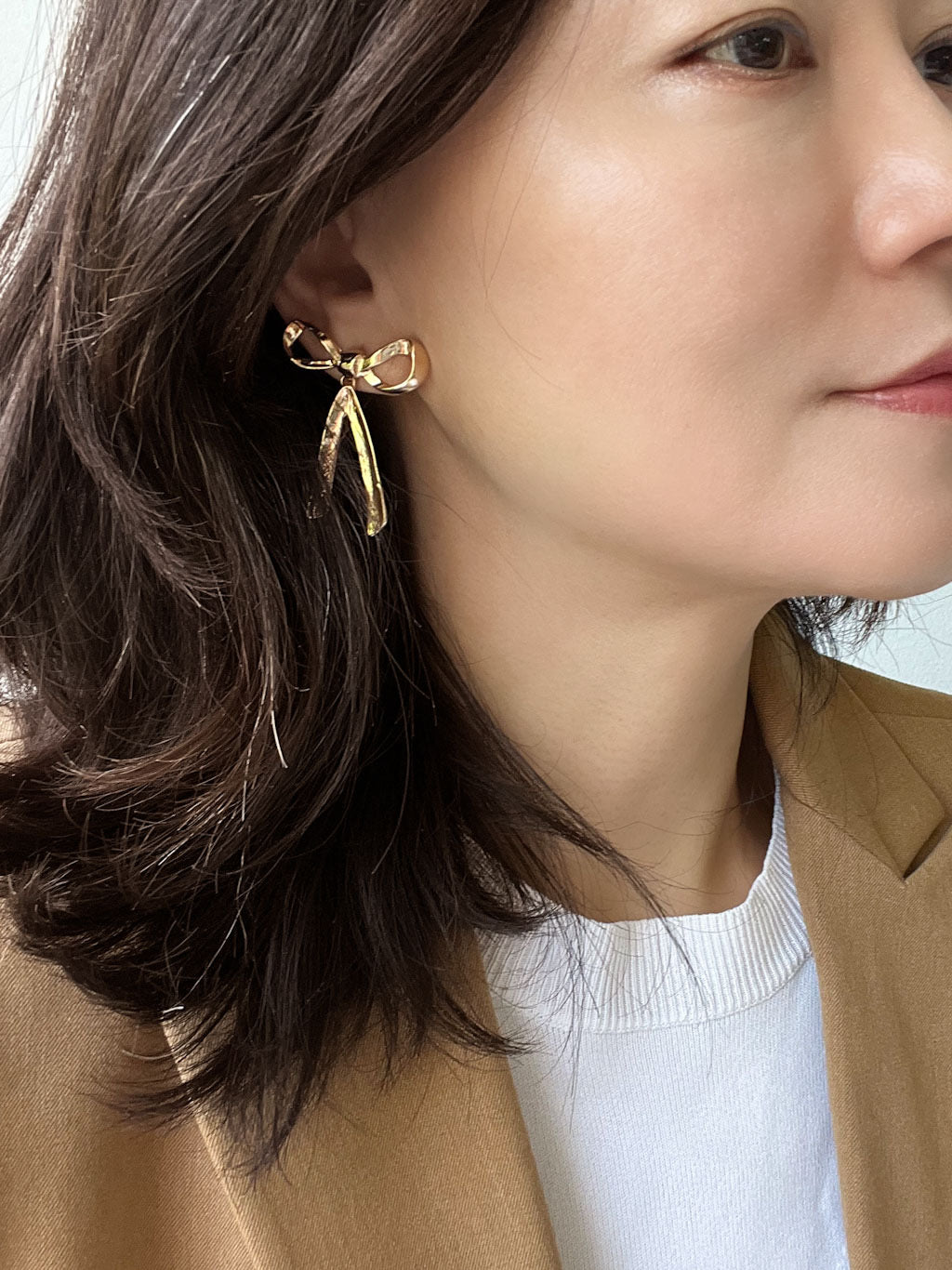 A pair of shiny gold-tone ribbon-shaped statement earrings with dangling lower ribbons.
