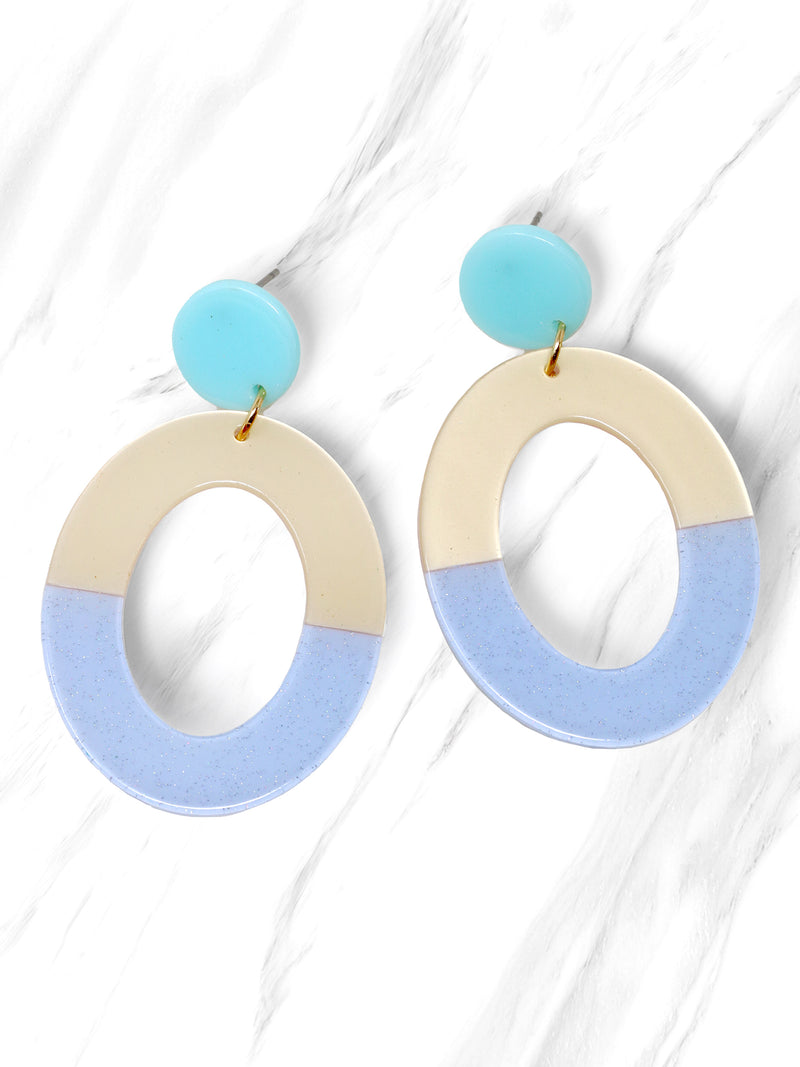 A pair of two-tone oval resin drop earrings with aqua blue studs and cream and glittery light blue oval dangles.