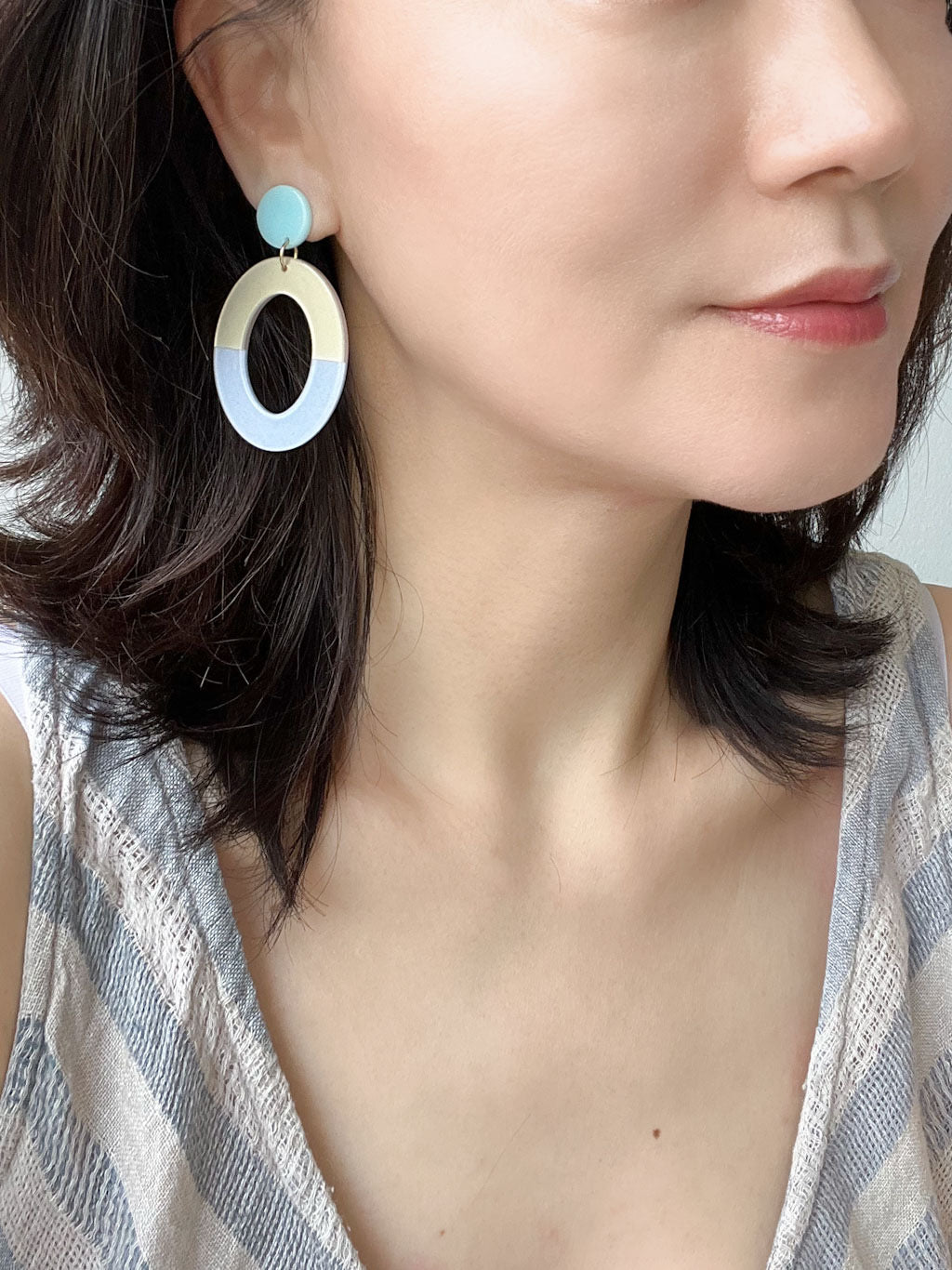 A pair of two-tone oval resin drop earrings with aqua blue studs and cream and glittery light blue oval dangles.