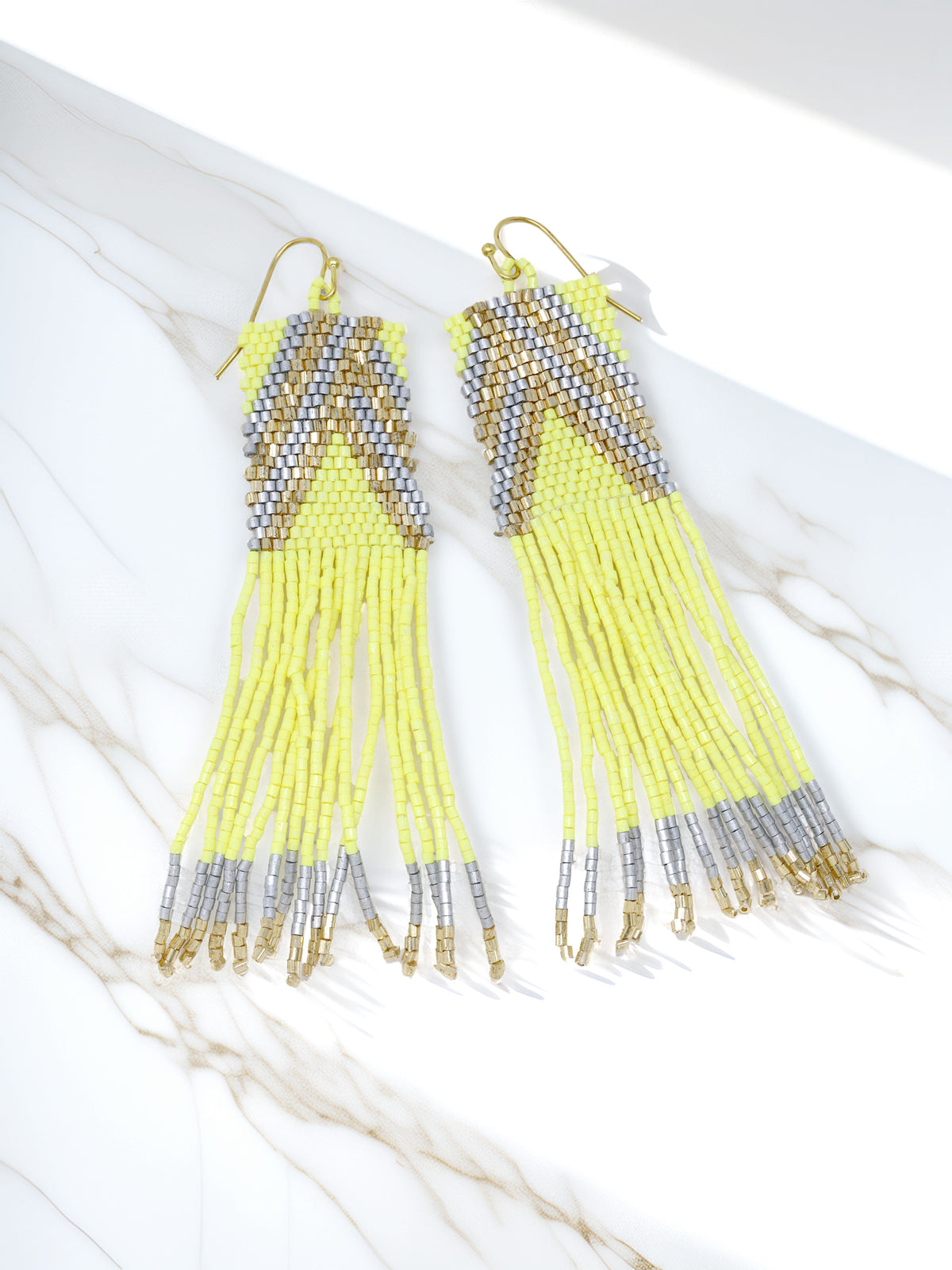 A pair of long seed beaded tassel earrings with a lime green, gold, and silver chevron pattern and dangling fringe strands.