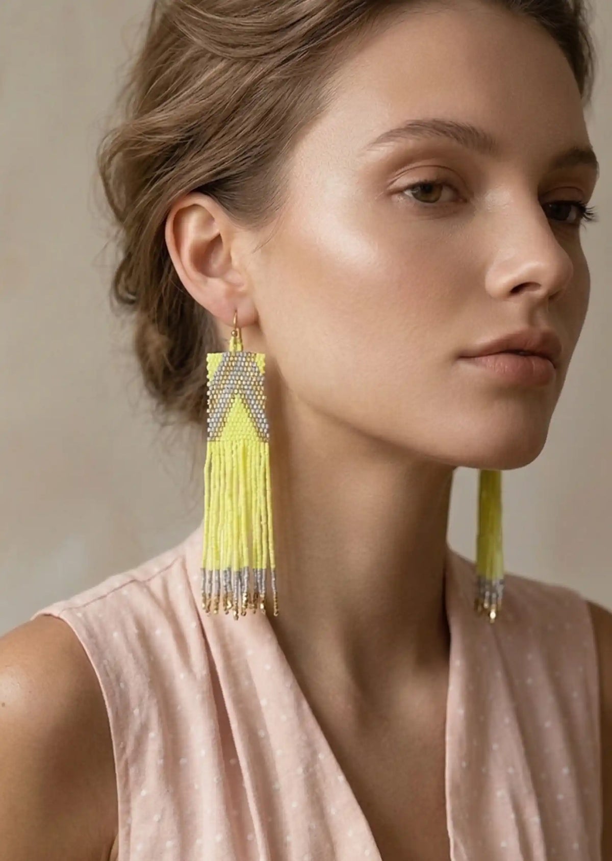 Woman wearing yellow tassel earrings against a neutral background