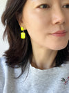 Neon yellow rectangle-shaped glass stone drop earrings with faceted detailing, set in gold-tone metal, displayed on a white earring stand.
