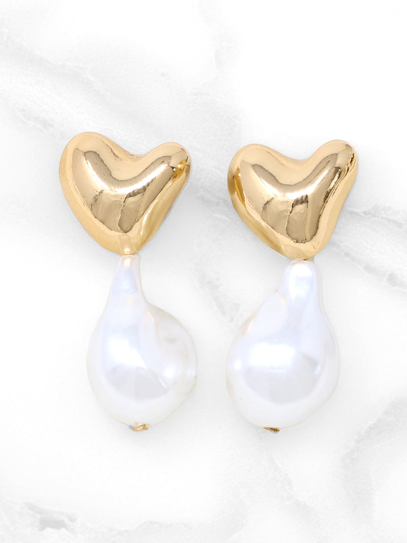 A pair of elegant earrings featuring polished gold-tone puffy heart studs with dangling irregular baroque pearls. The earrings are displayed on a white jewelry stand against a clean background, showcasing their modern yet timeless design.