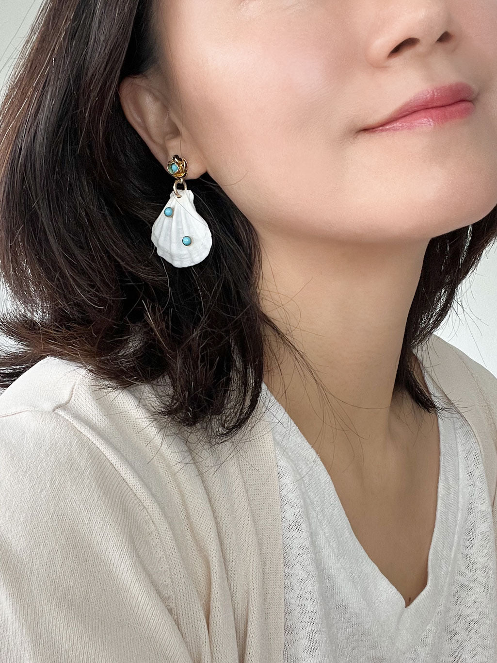 A pair of white natural shell drop earrings featuring turquoise accent stones and gold floral studs.