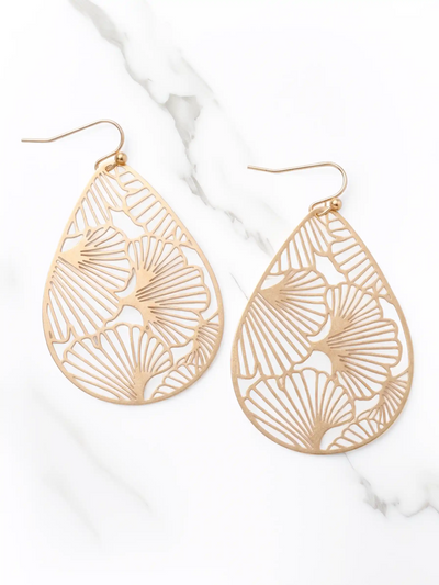 Gold teardrop-shaped earrings with intricate patterns on a white marble surface